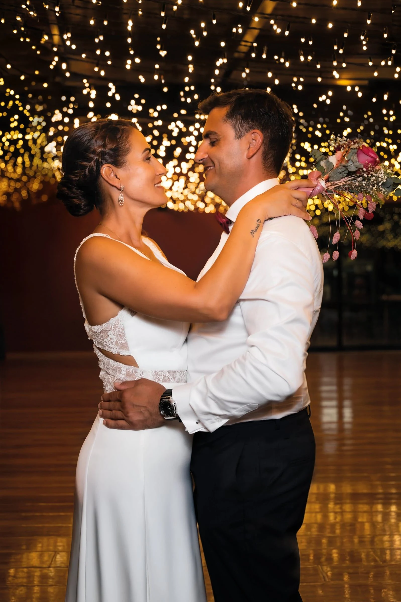 Pareja bailando abrazada bajo una guirnalda de luces.