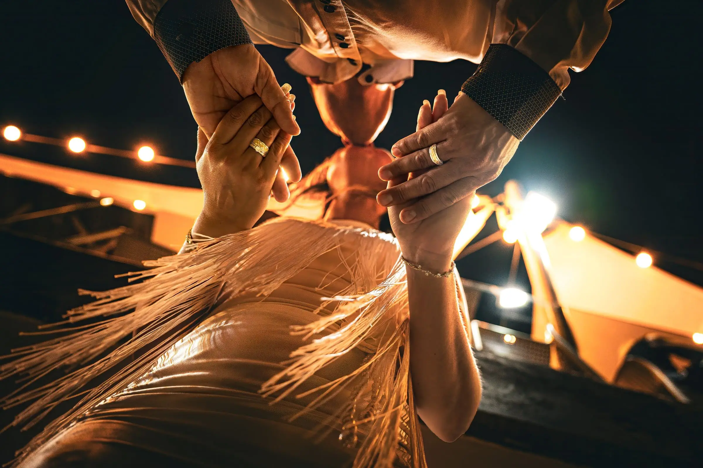 Novios bailando entre luces cálidas, fotografiados desde un ángulo bajo.