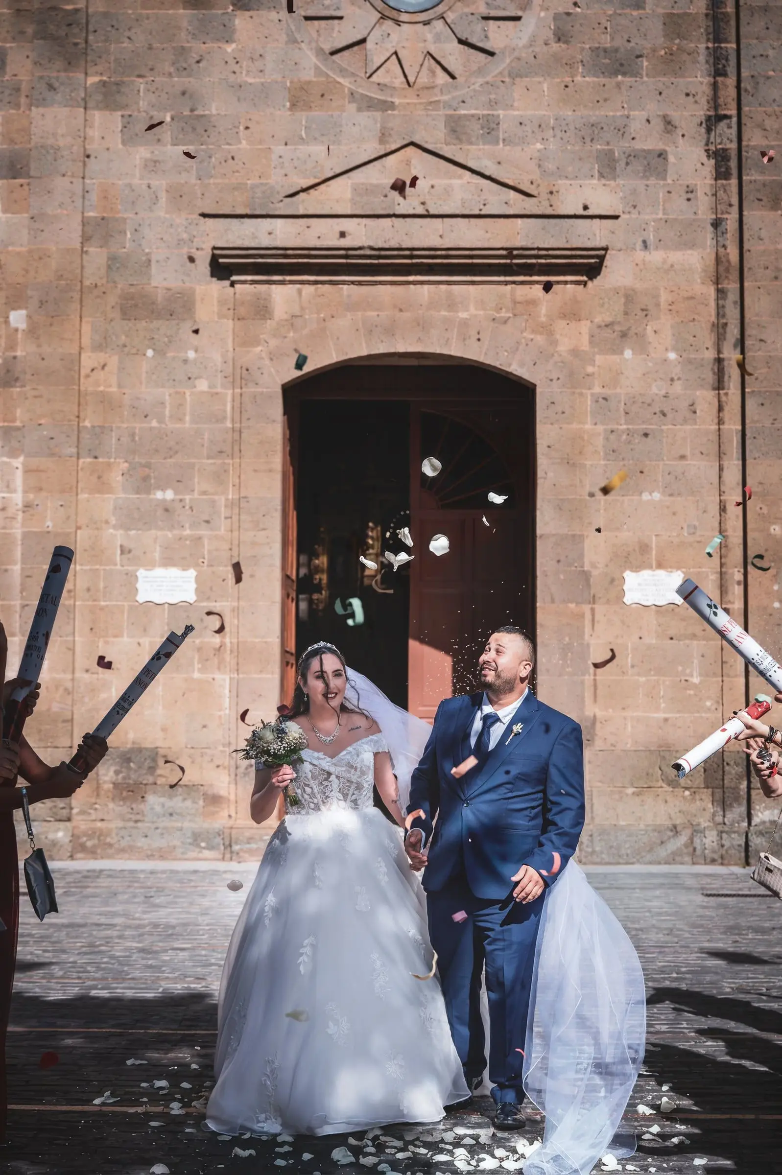 Novios saliendo de la iglesia entre confeti y cintas blancas.
