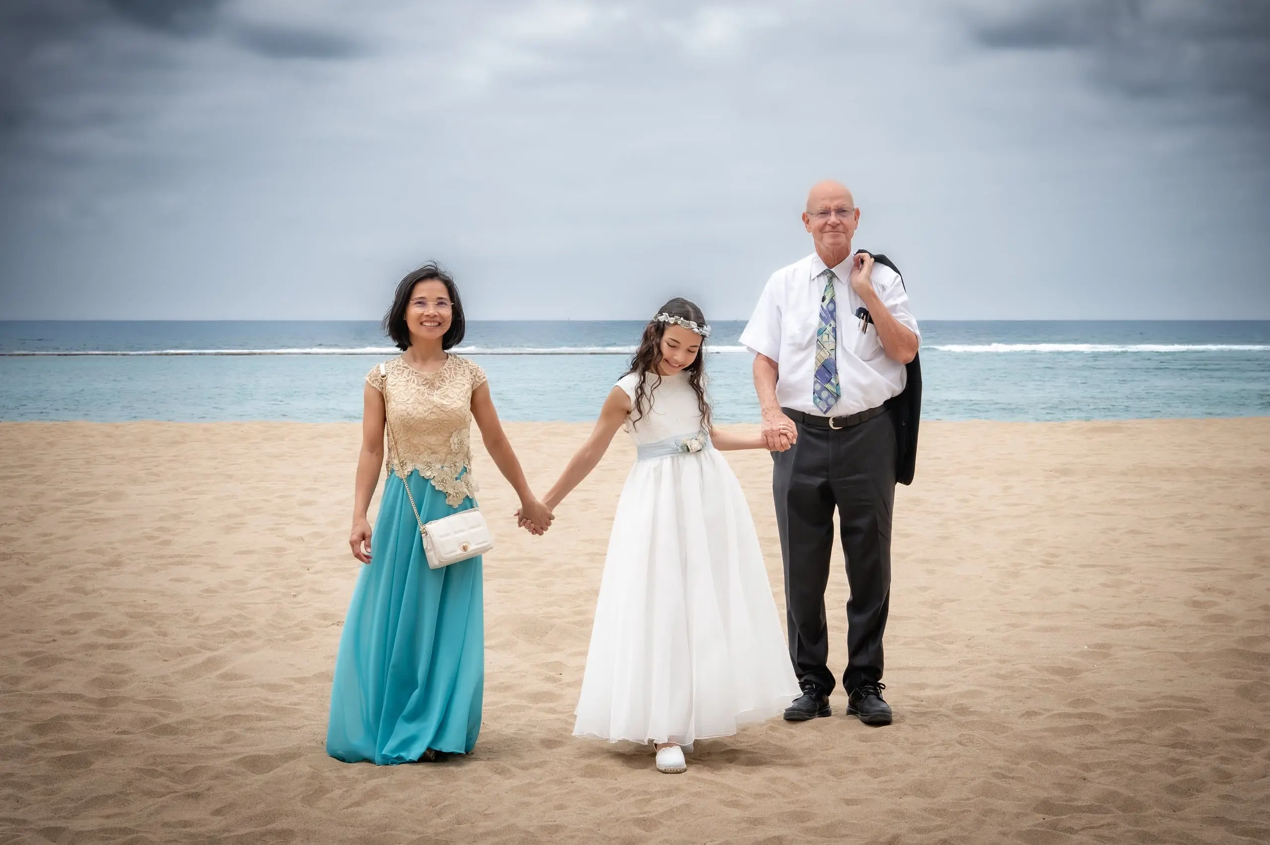 Niña de comunión caminando de la mano de sus abuelos por una playa de Gran Canaria.