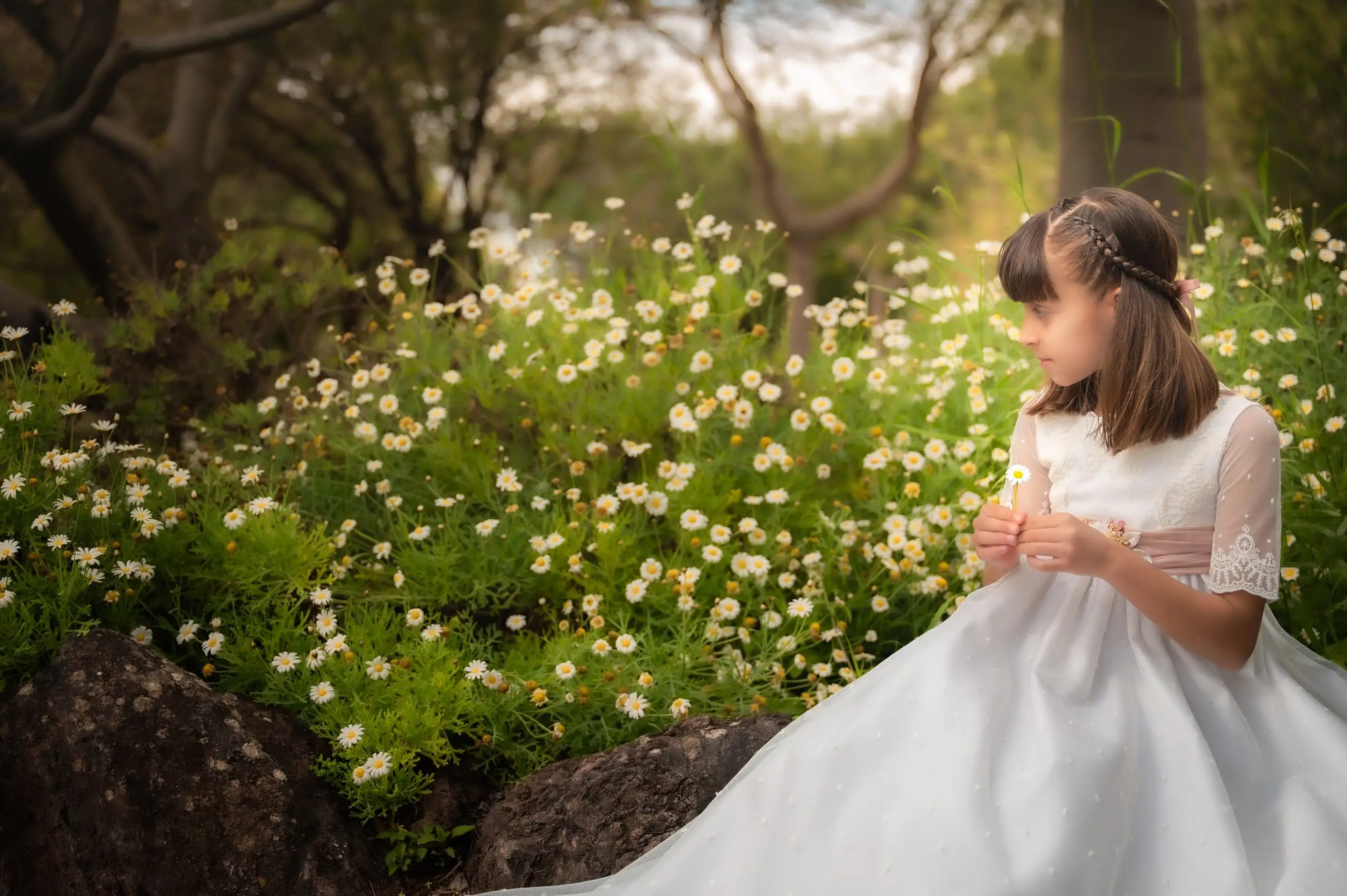 Niña de comunión observando unas flores blancas en un jardín de Gran Canaria.