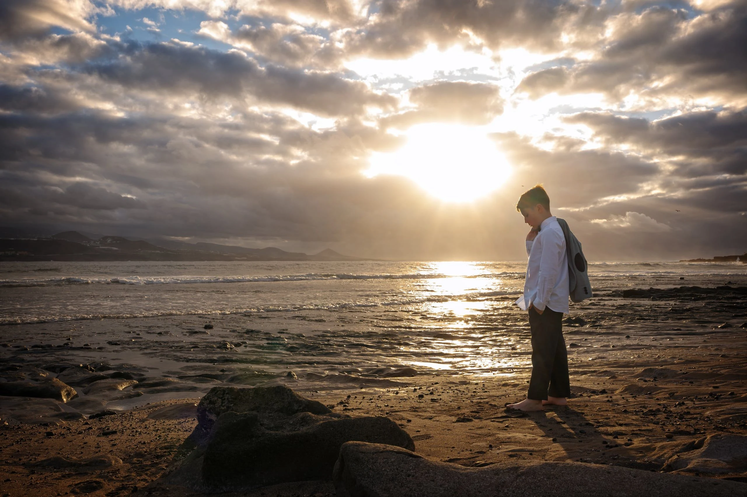 Niño de comunión contemplando el mar al atardecer en Gran Canaria.