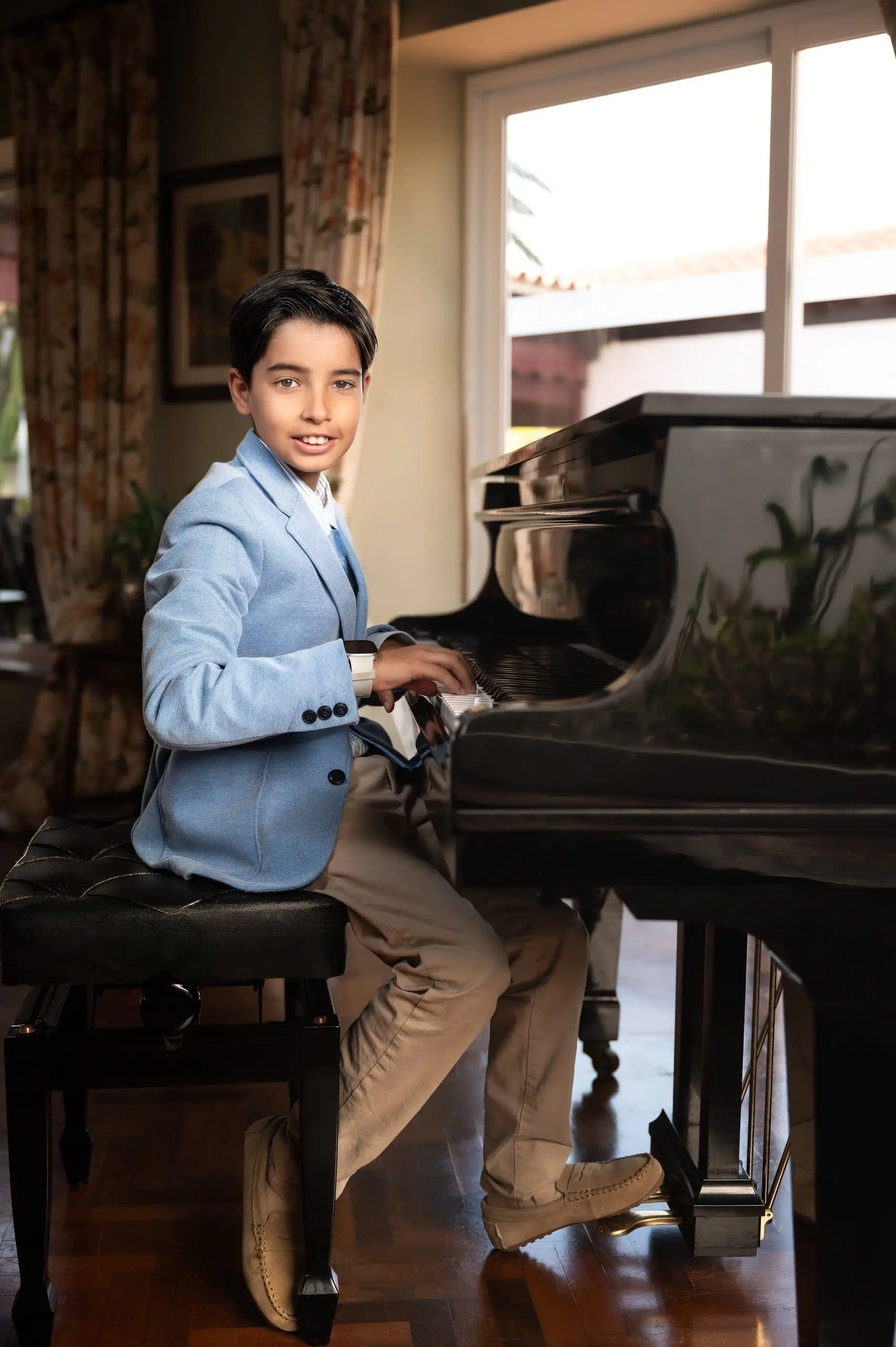 Niño de comunión tocando un piano y mirando a cámara con naturalidad.