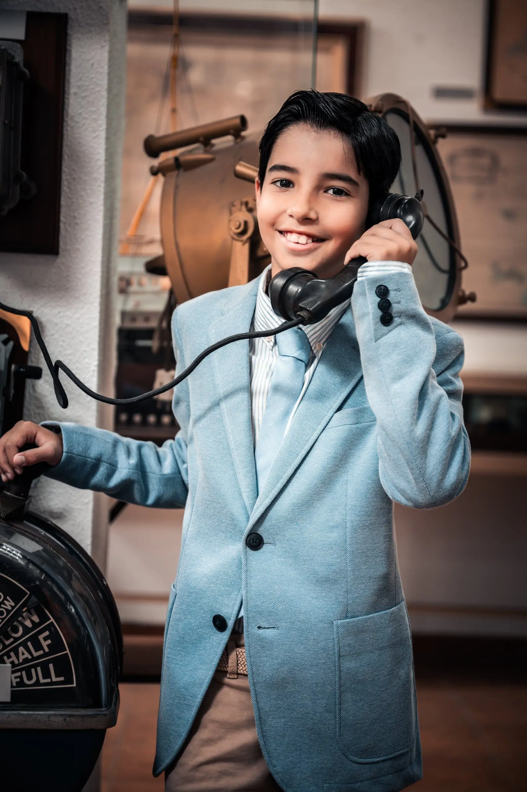 Niño con traje azul jugando con un teléfono antiguo durante su reportaje de comunión.