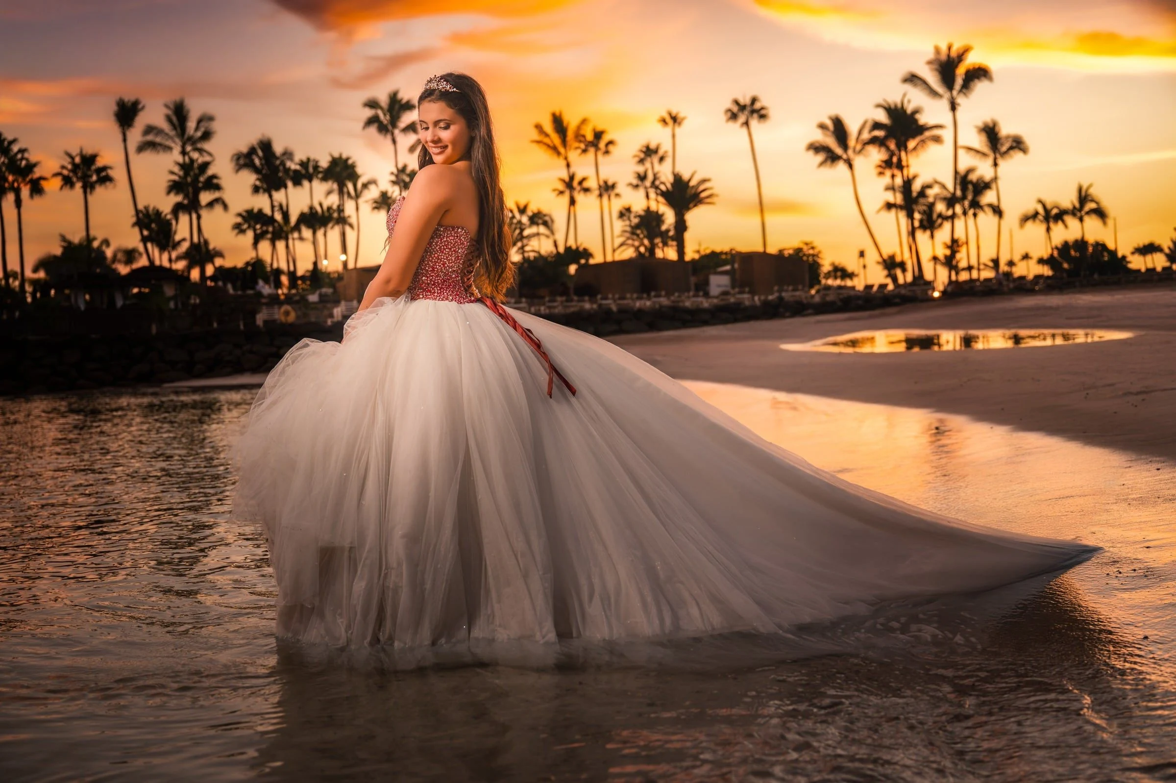 Quinceañera con vestido blanco junto al agua al atardecer.