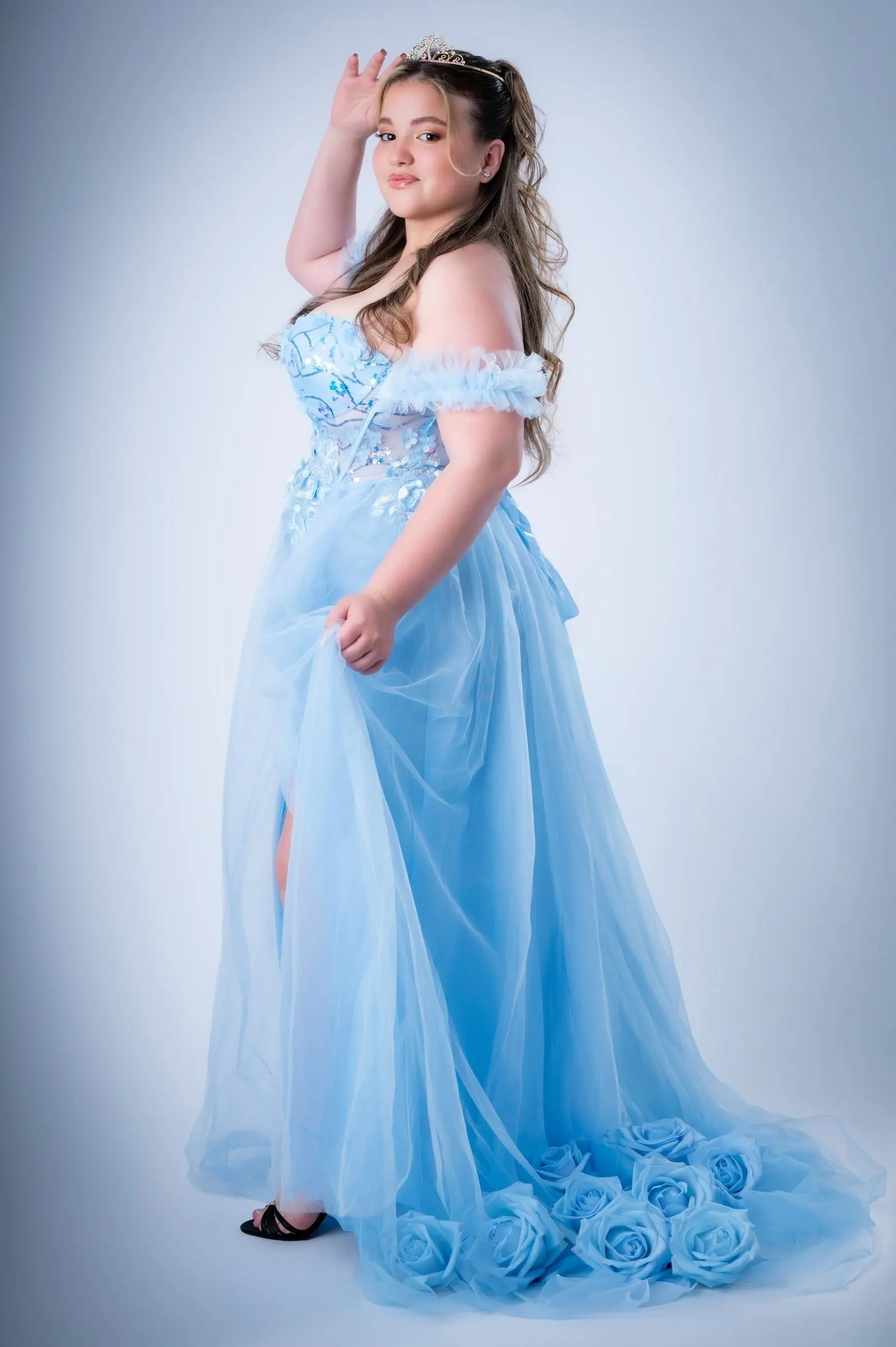 Joven con vestido azul largo y corona, de pie en el estudio.