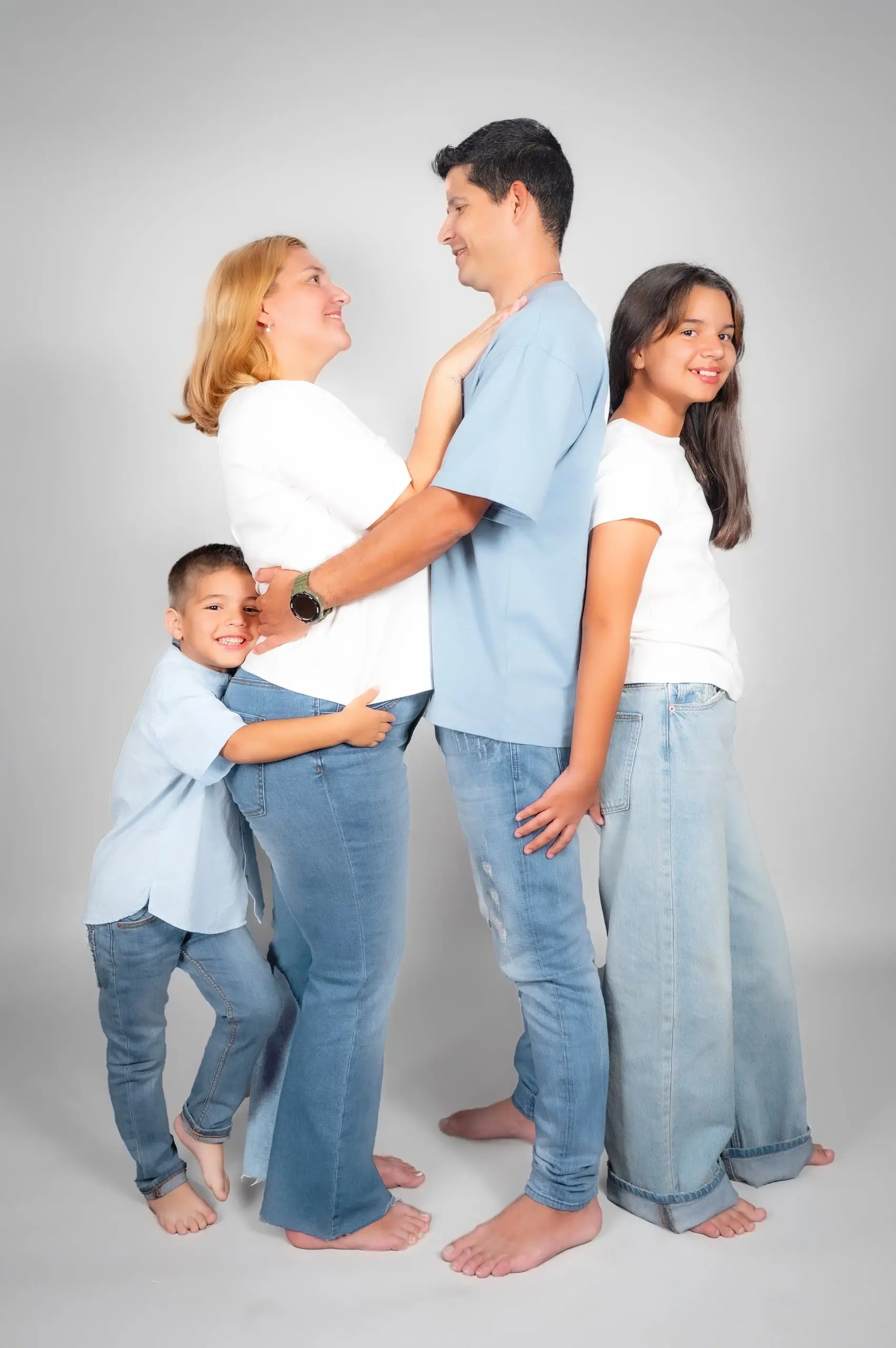 Familia de cuatro personas abrazada en un retrato de estudio.