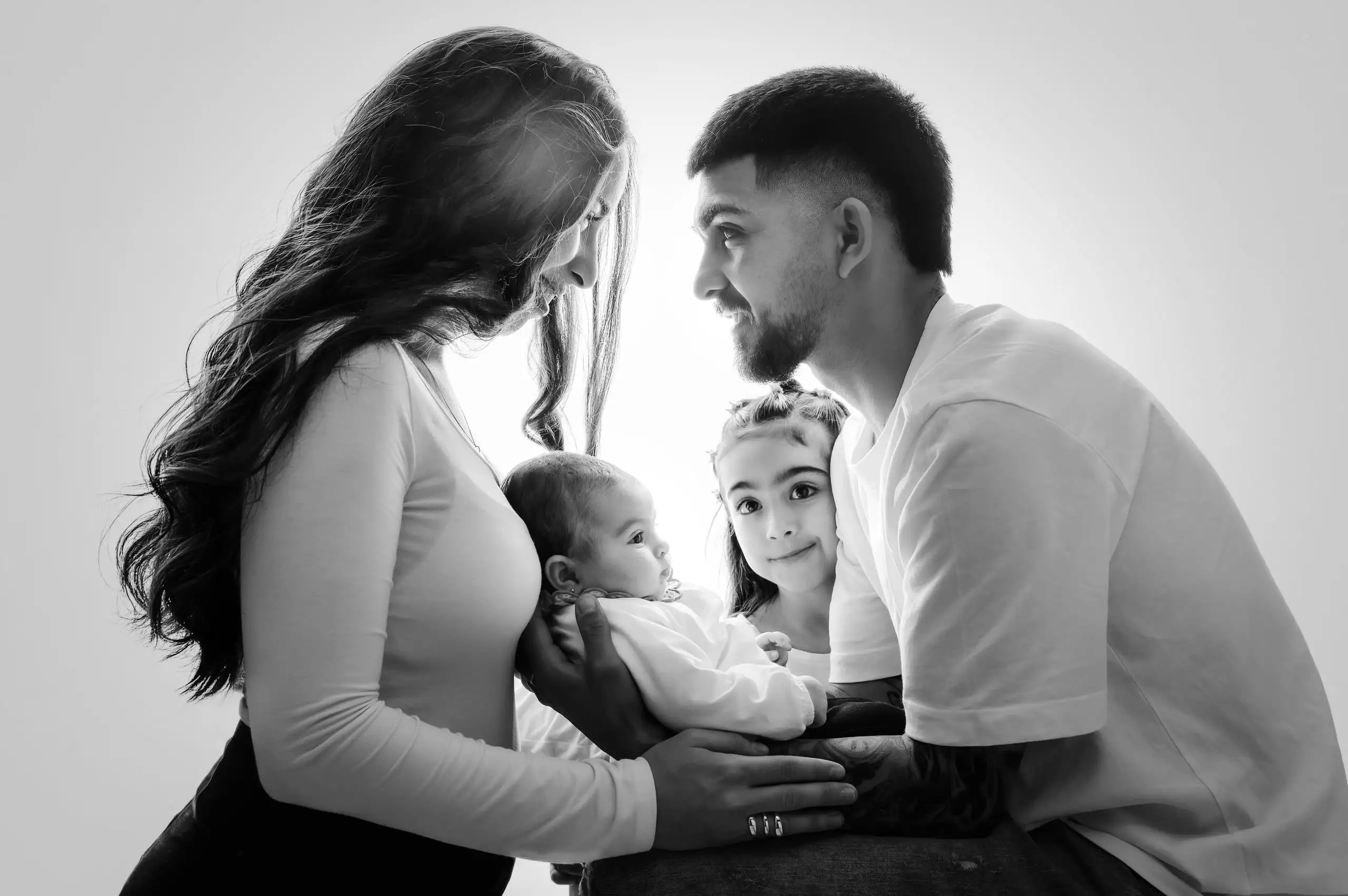 Padres y hermana mirando al bebé durante una sesión familiar en blanco y negro.