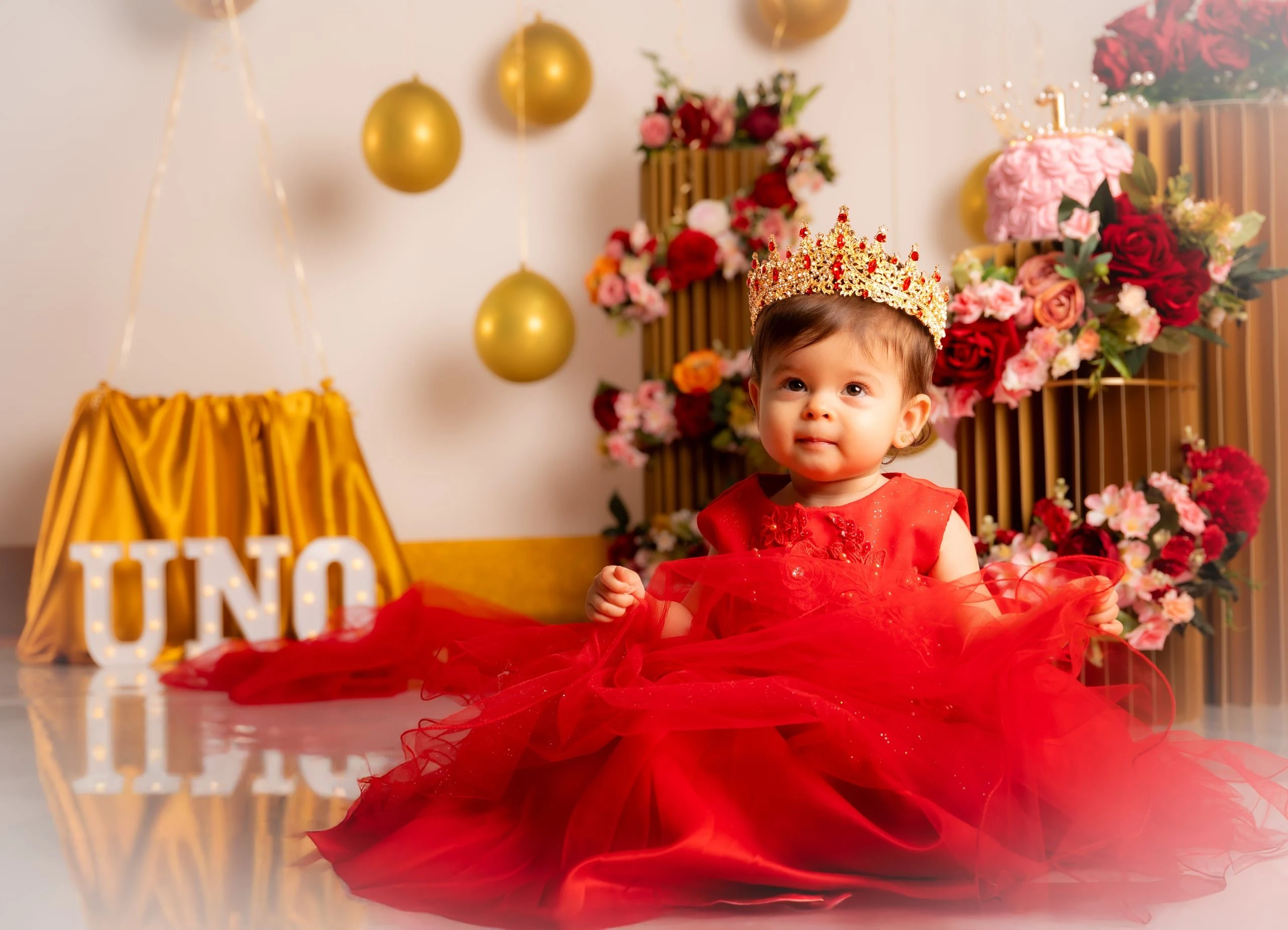 Niña con vestido rojo y corona en un decorado de primer cumpleaños.