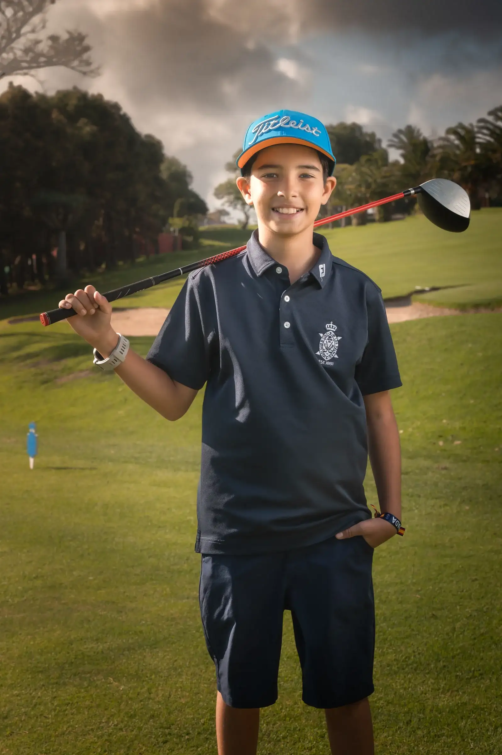 Niño con gorra y un palo de golf sobre los hombros en el césped.