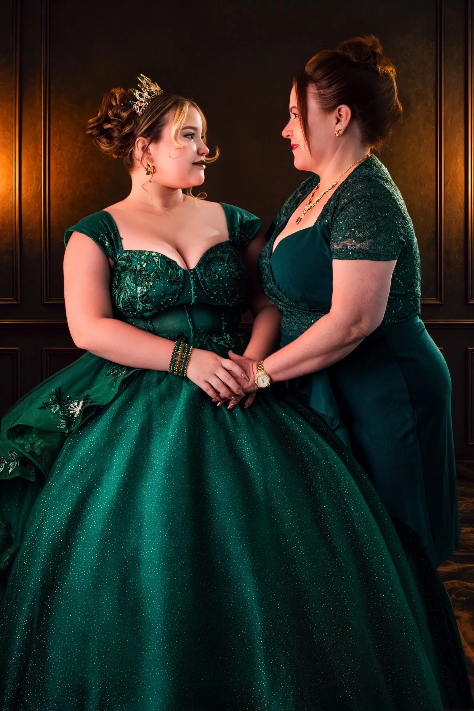 Quinceañera y su madre se miran con vestidos verdes en el estudio.