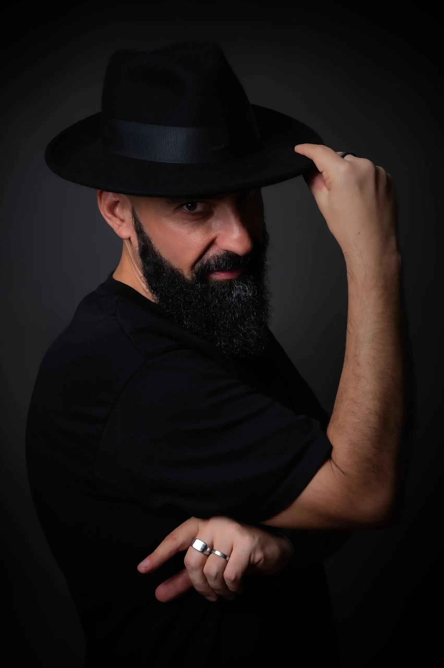 Retrato vertical de un hombre con sombrero, iluminado sobre fondo oscuro.
