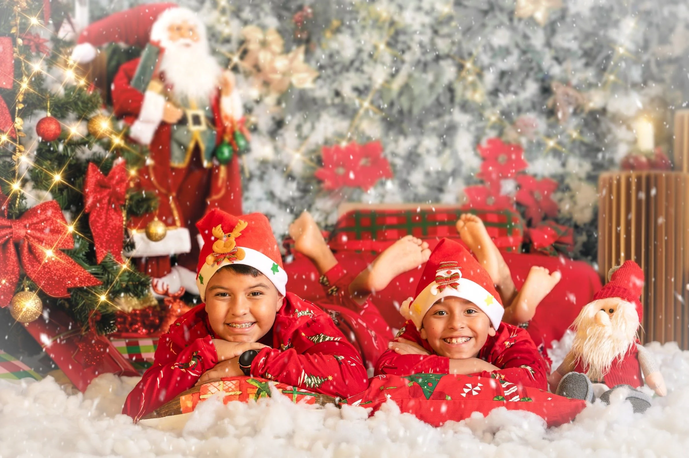 Dos niños con pijamas rojos tumbados en la nieve del decorado navideño.