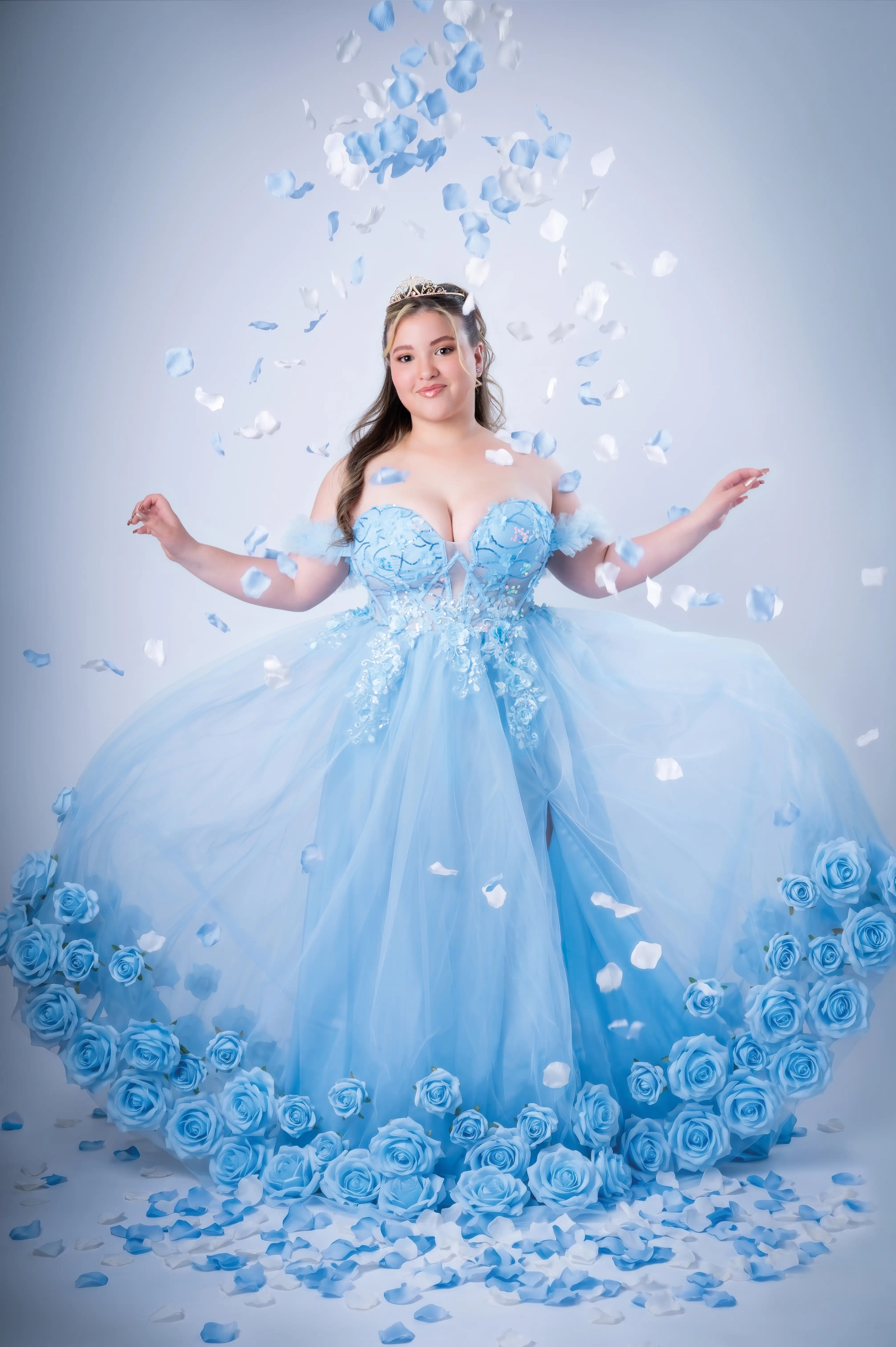 Quinceañera con vestido azul claro y pétalos en un escenario de estudio.