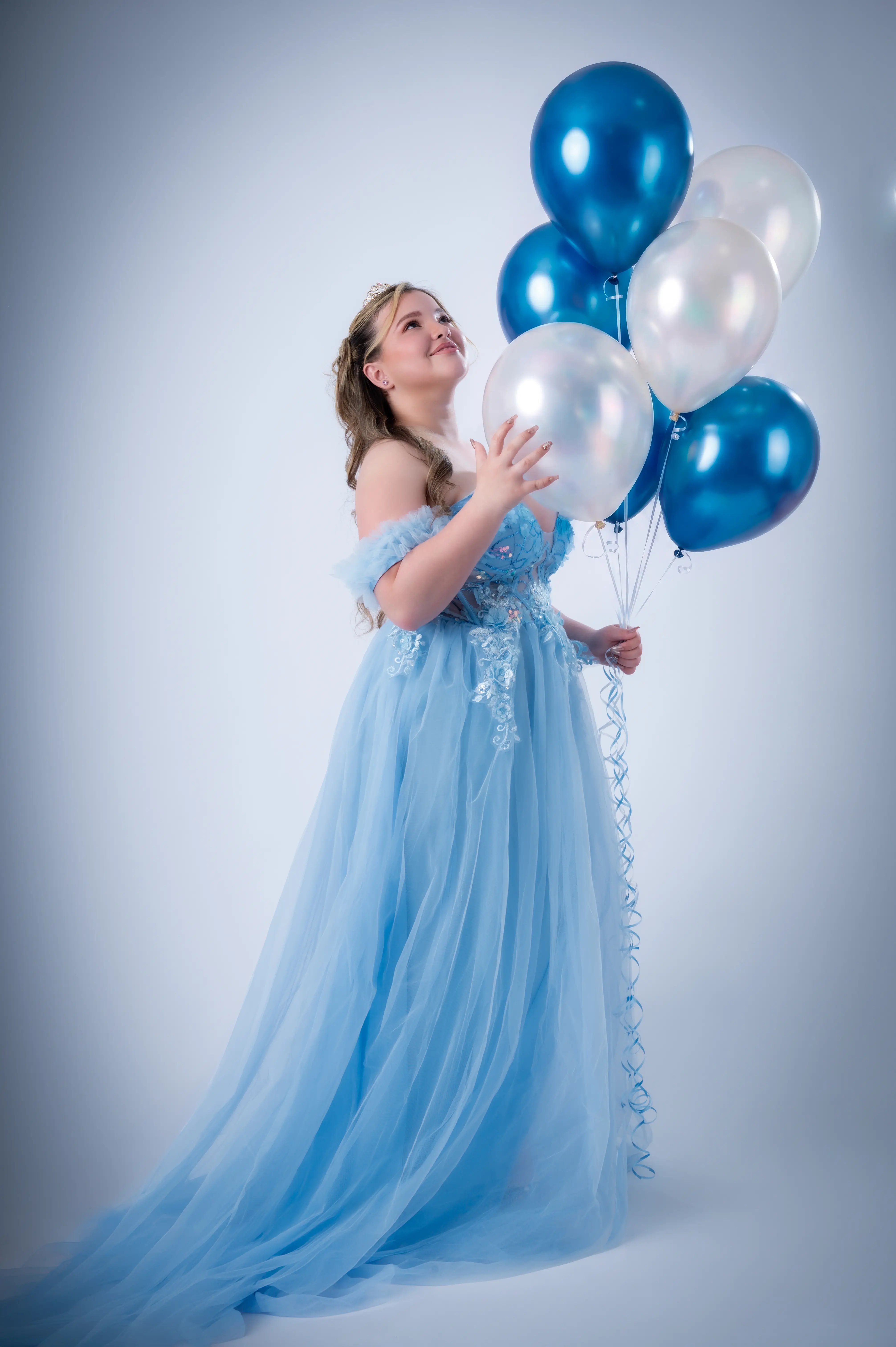Quinceañera con vestido azul claro y globos de colores suaves en el estudio.