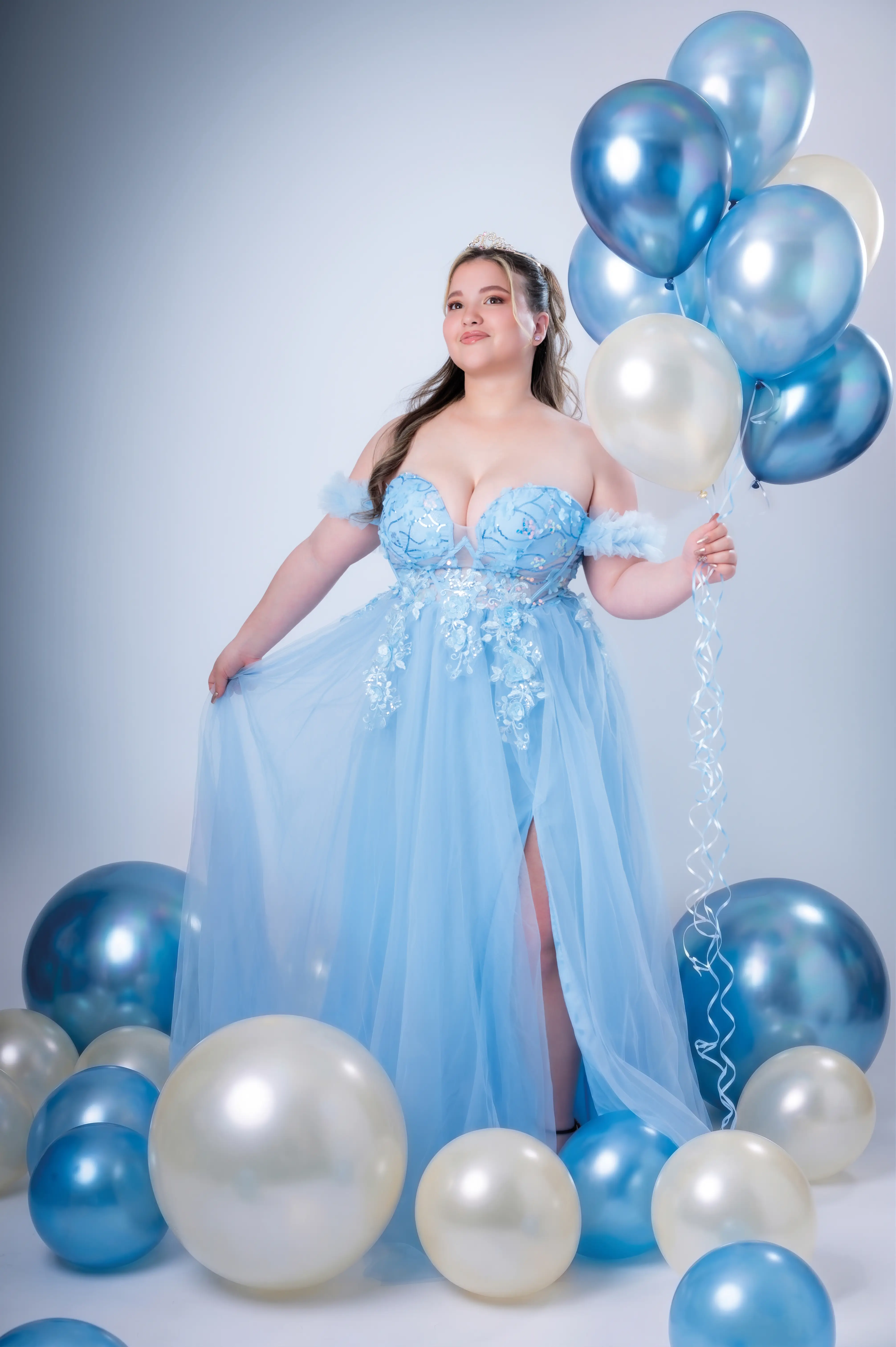 Quinceañera con vestido azul claro rodeada de globos y luz suave.