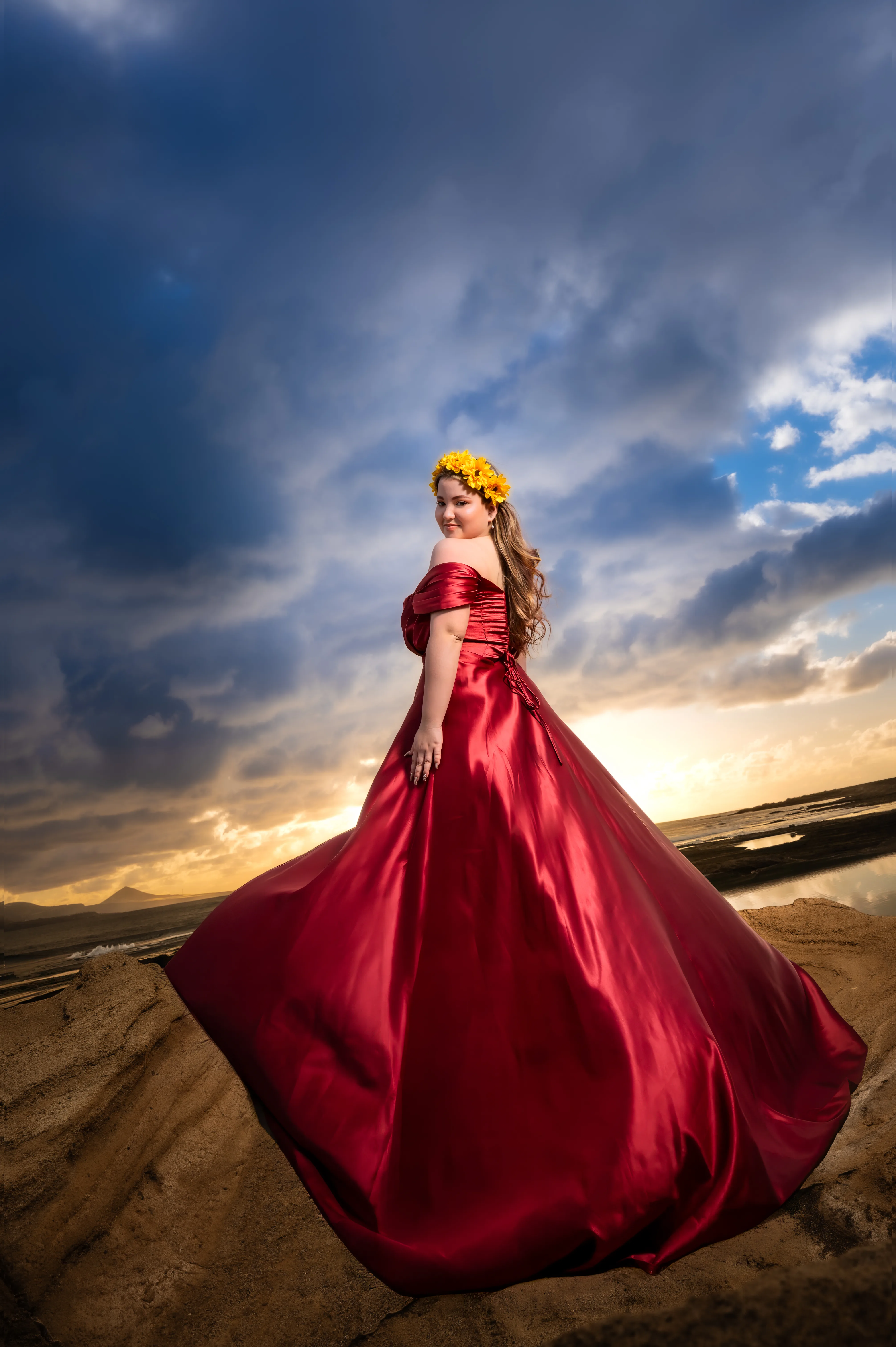 Quinceañera con vestido rojo junto al mar bajo un cielo de nubes.