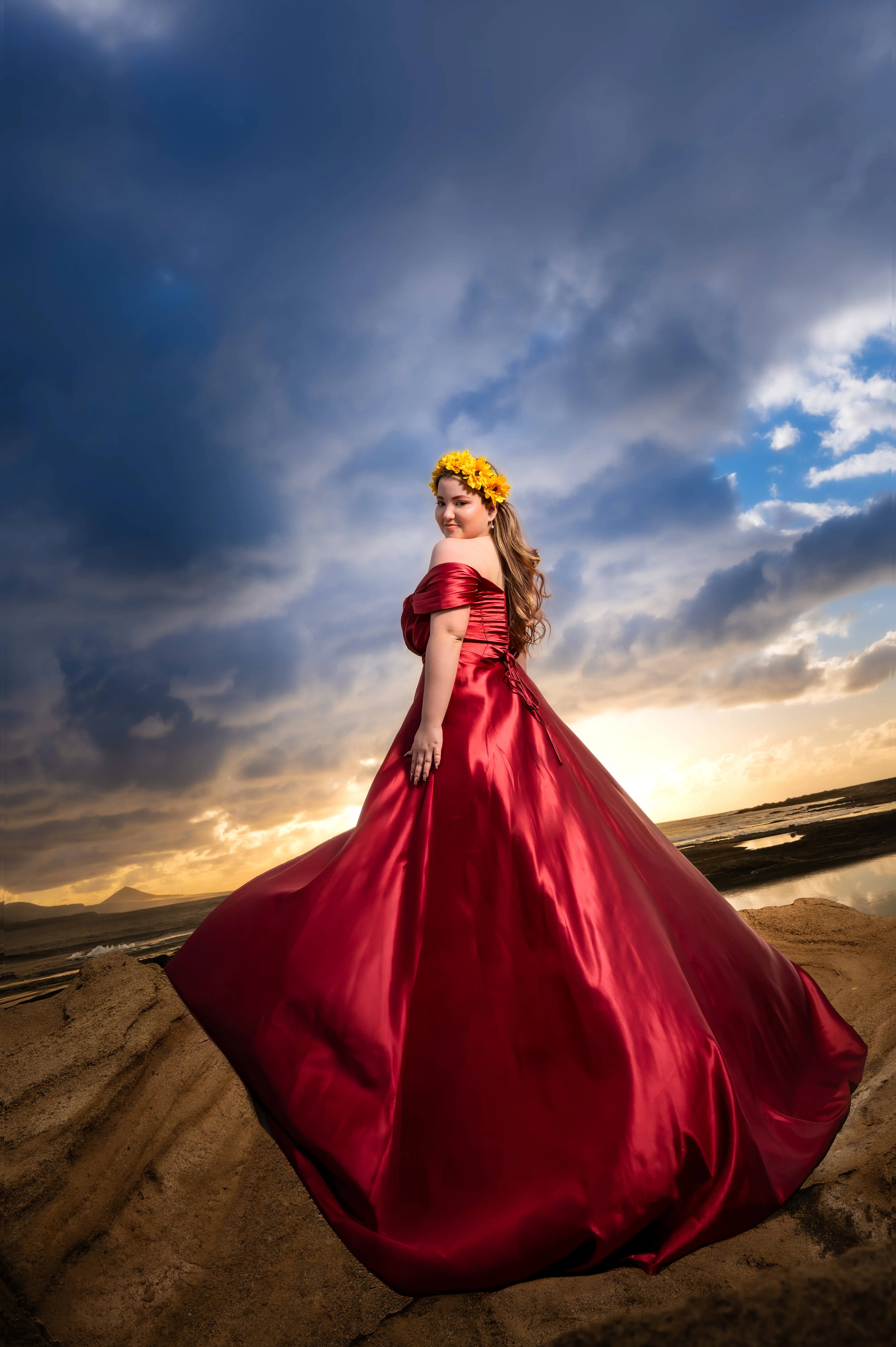 Quinceañera con vestido rojo junto al mar bajo un cielo de nubes.
