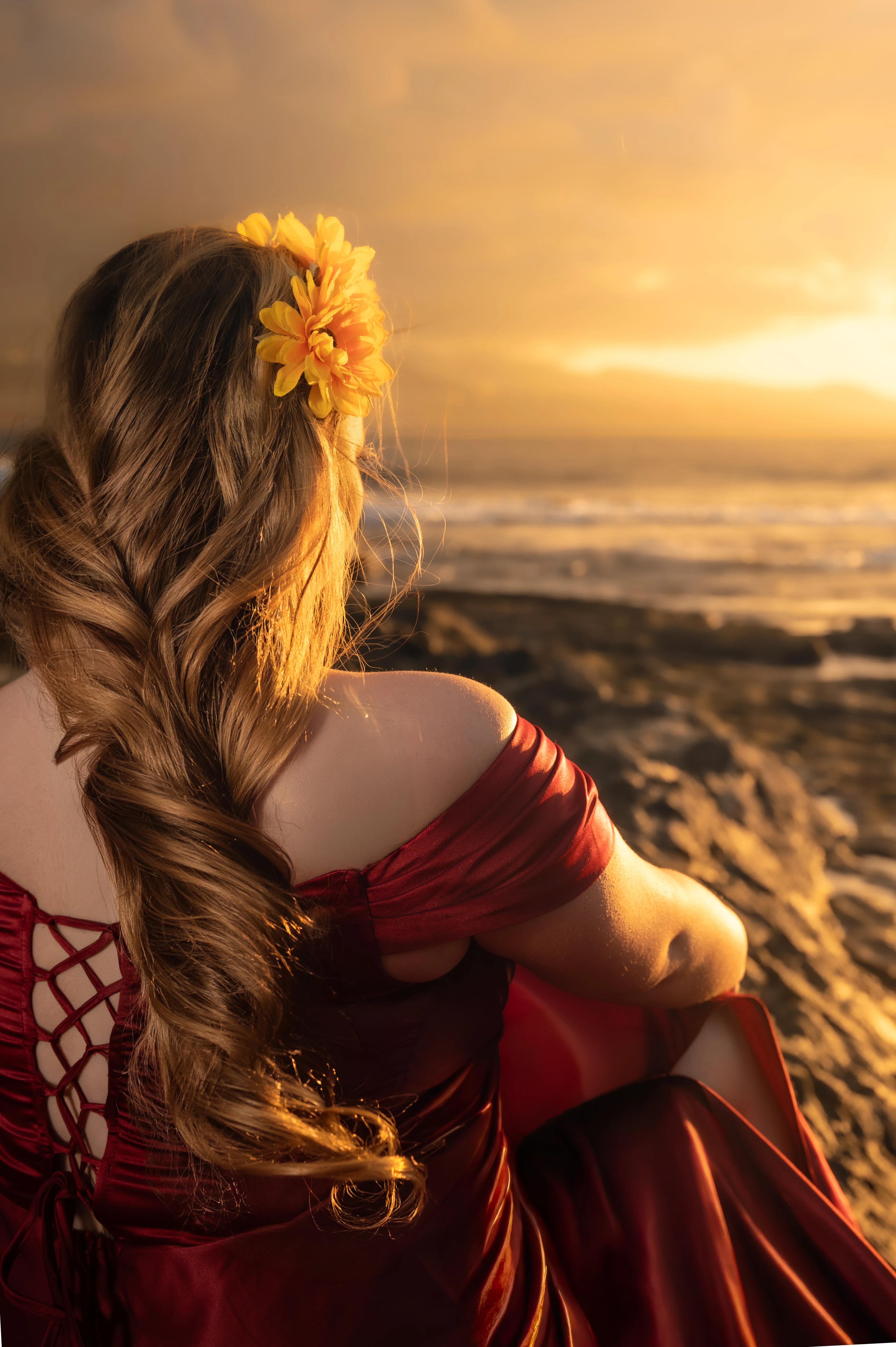 Retrato de quinceañera con vestido rojo iluminada por el atardecer junto al mar.