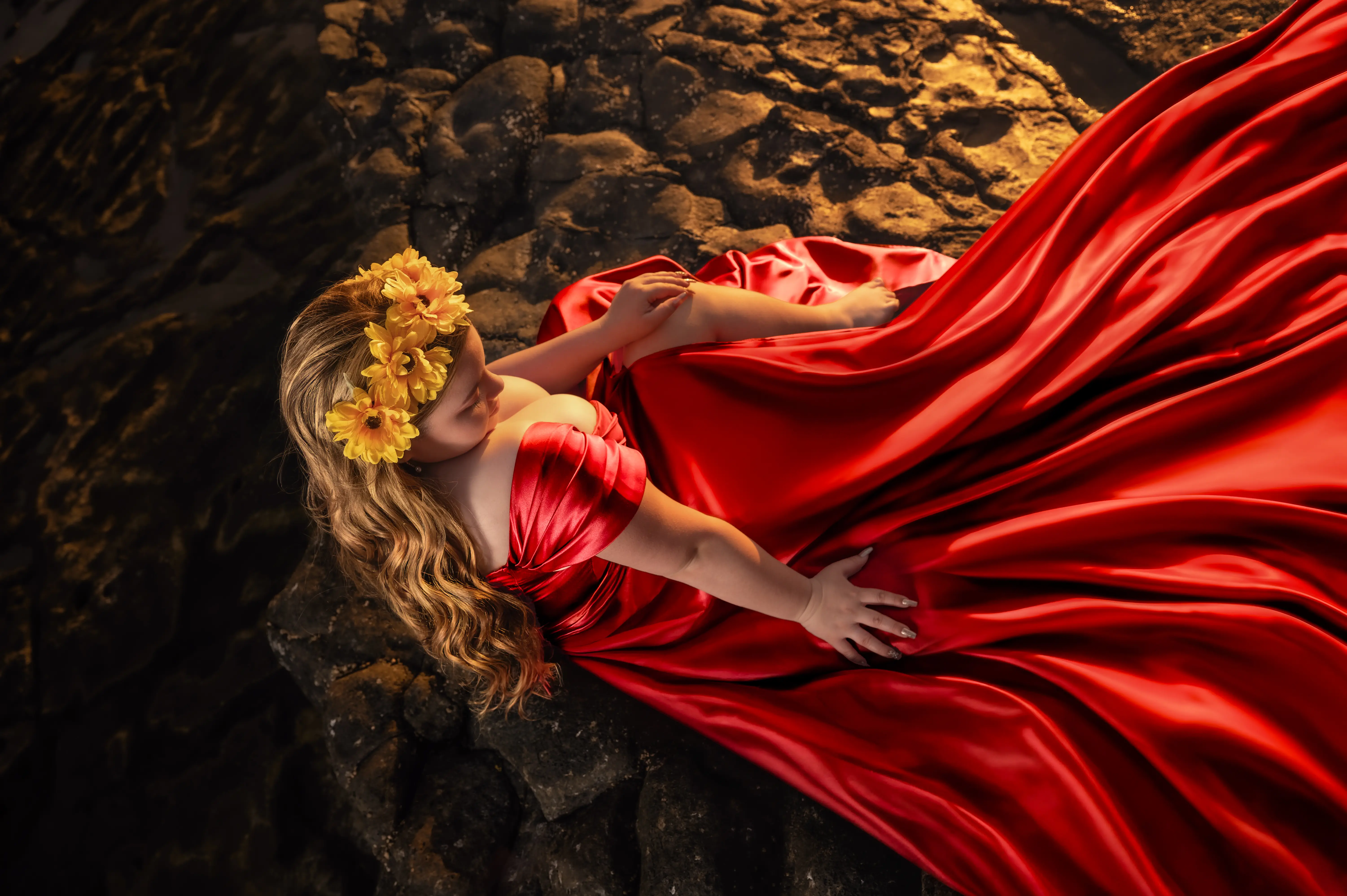 Quinceañera con vestido rojo extendido sobre las rocas junto al agua.