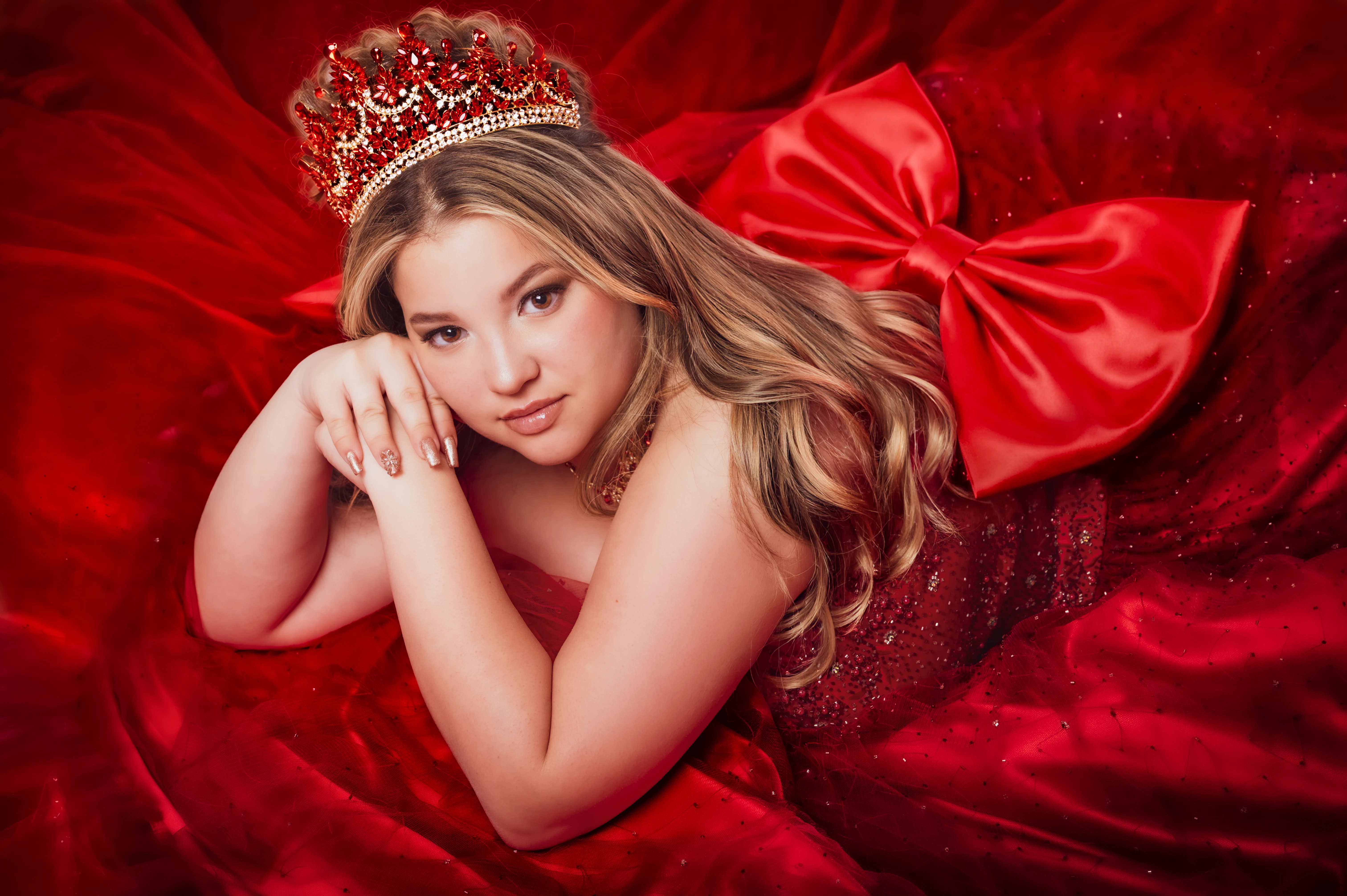 Retrato de quinceañera con corona roja sobre un fondo de tela roja.