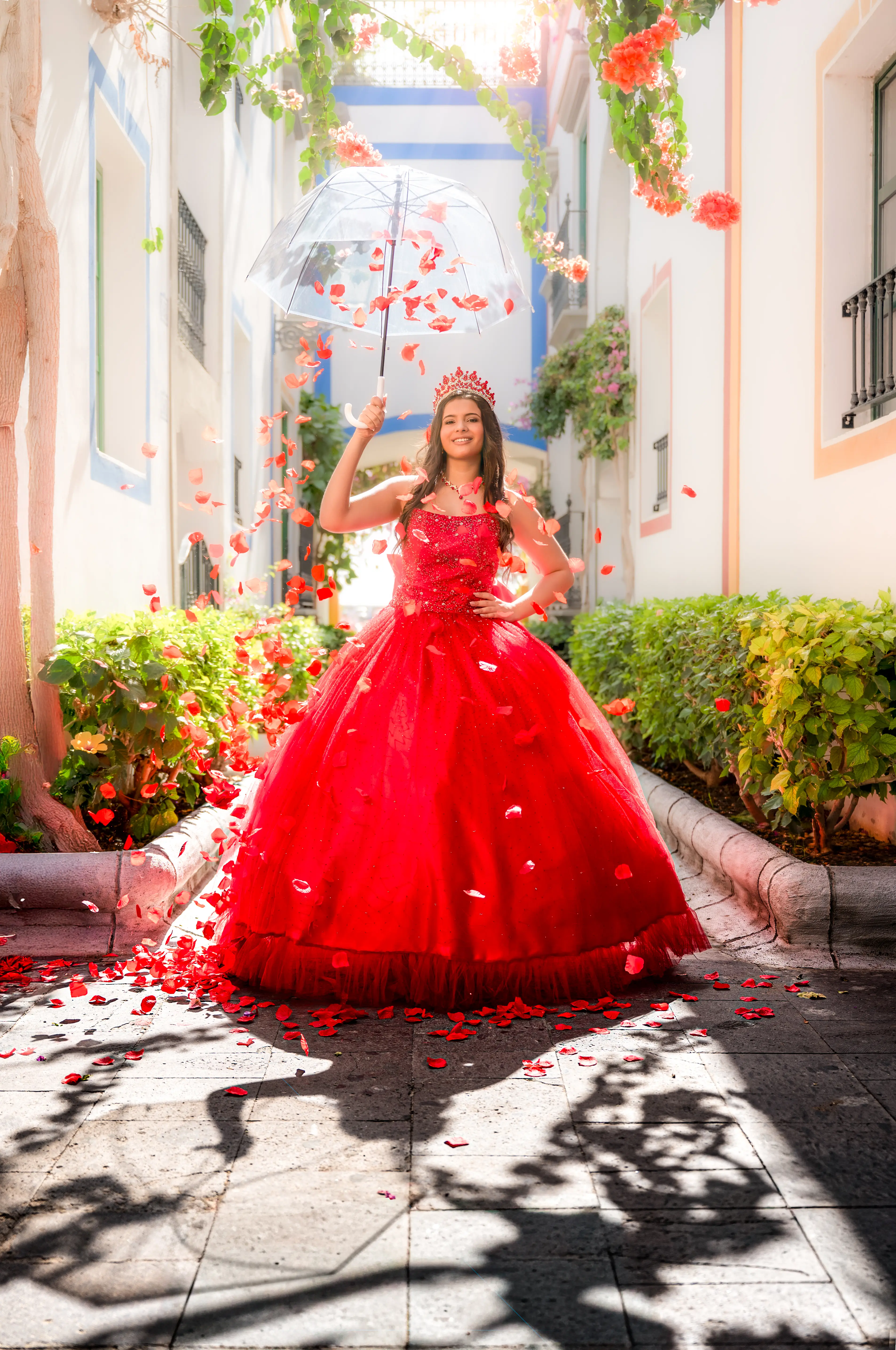 Quinceañera con vestido rojo bajo un paraguas mientras caen pétalos.