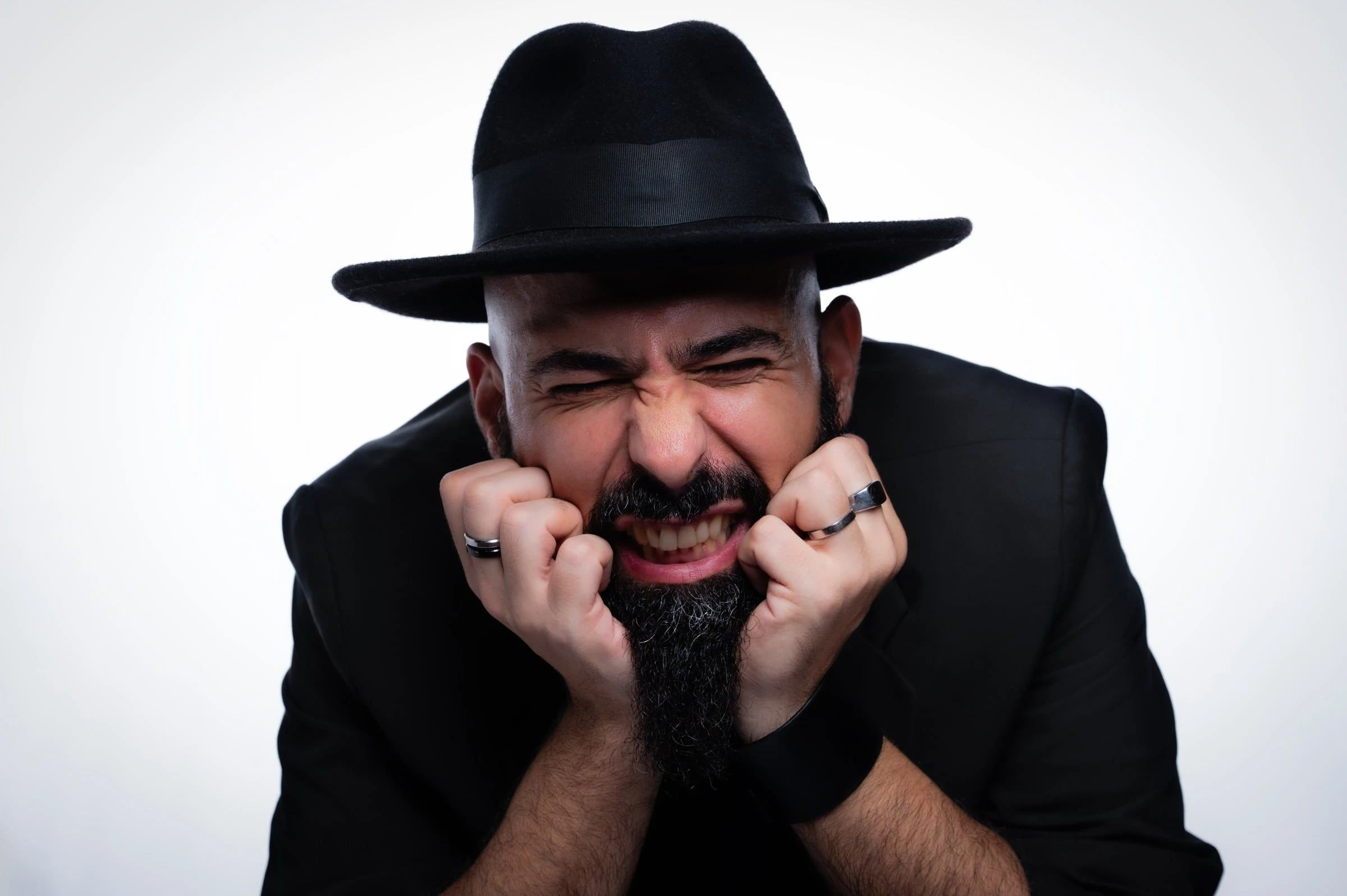Hombre con sombrero negro, sonriendo con las manos apoyadas en las mejillas.