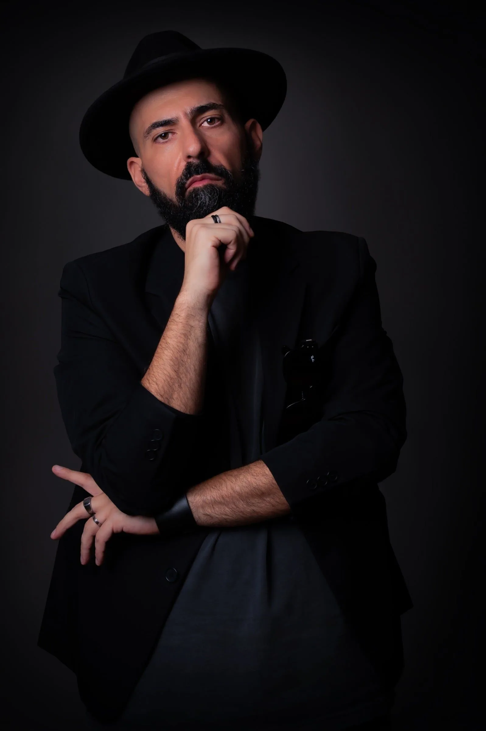Retrato de un hombre con sombrero y chaqueta negros, con una mano junto al mentón.