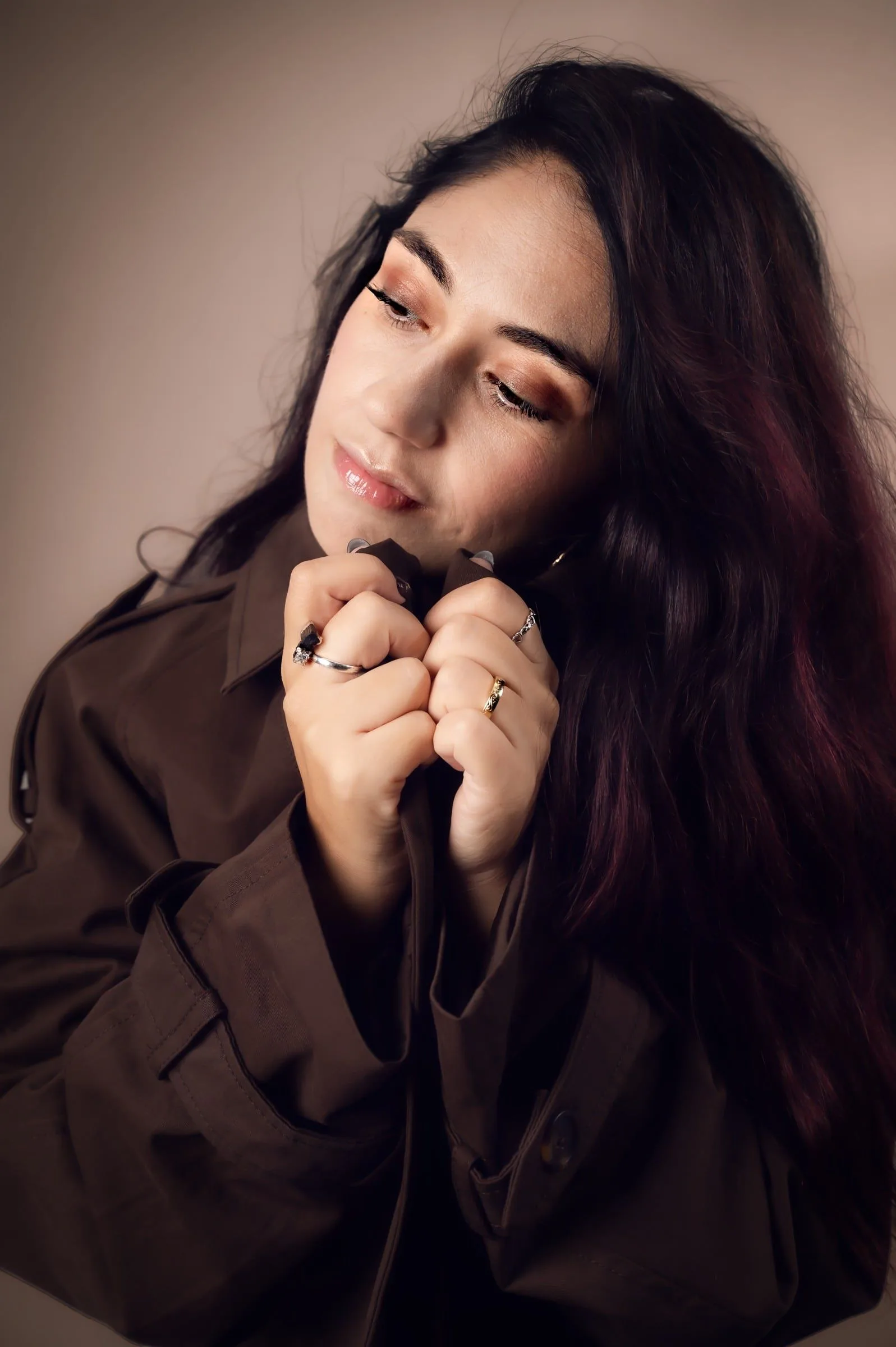 Retrato de una mujer con los ojos cerrados y las manos bajo el mentón, iluminada con luz suave.
