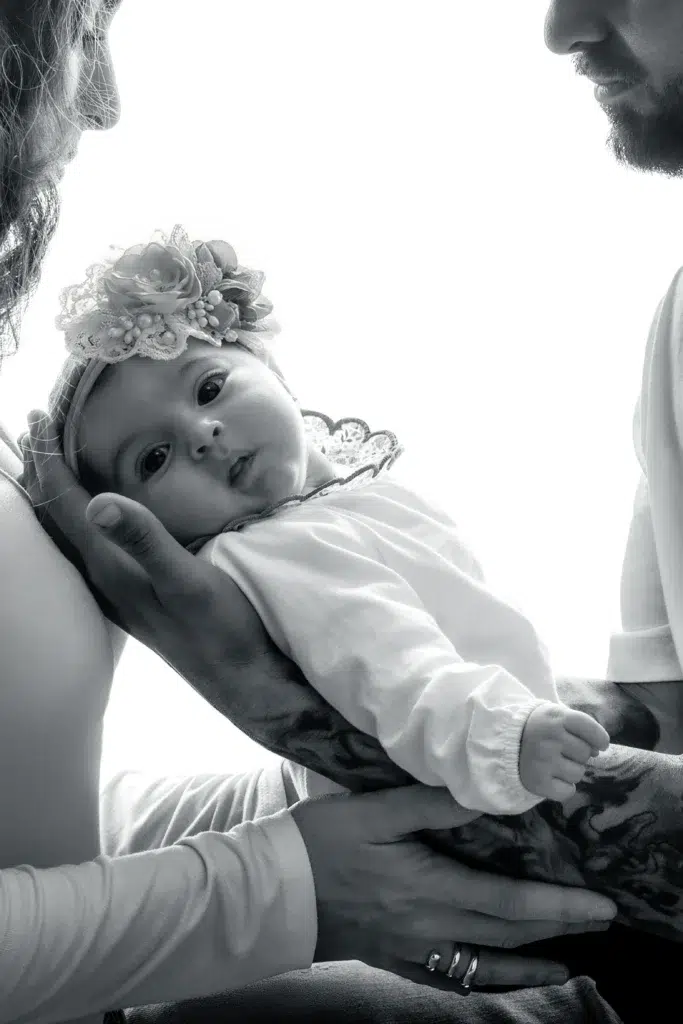 Bebé recién nacida sostenida por sus padres durante una sesión familiar en blanco y negro