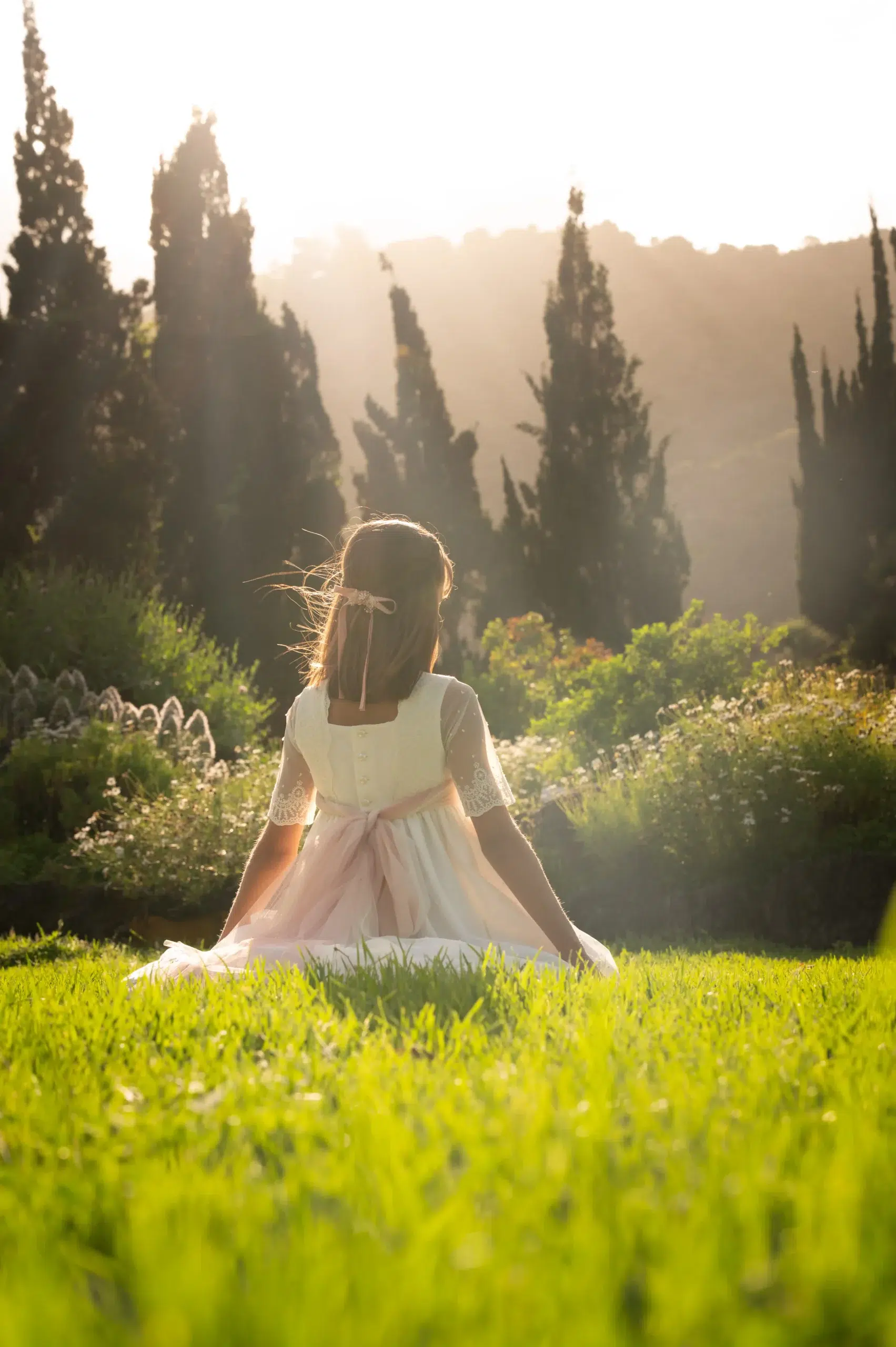 Niña con vestido de comunión sentada en un jardÃn iluminado por el atardecer