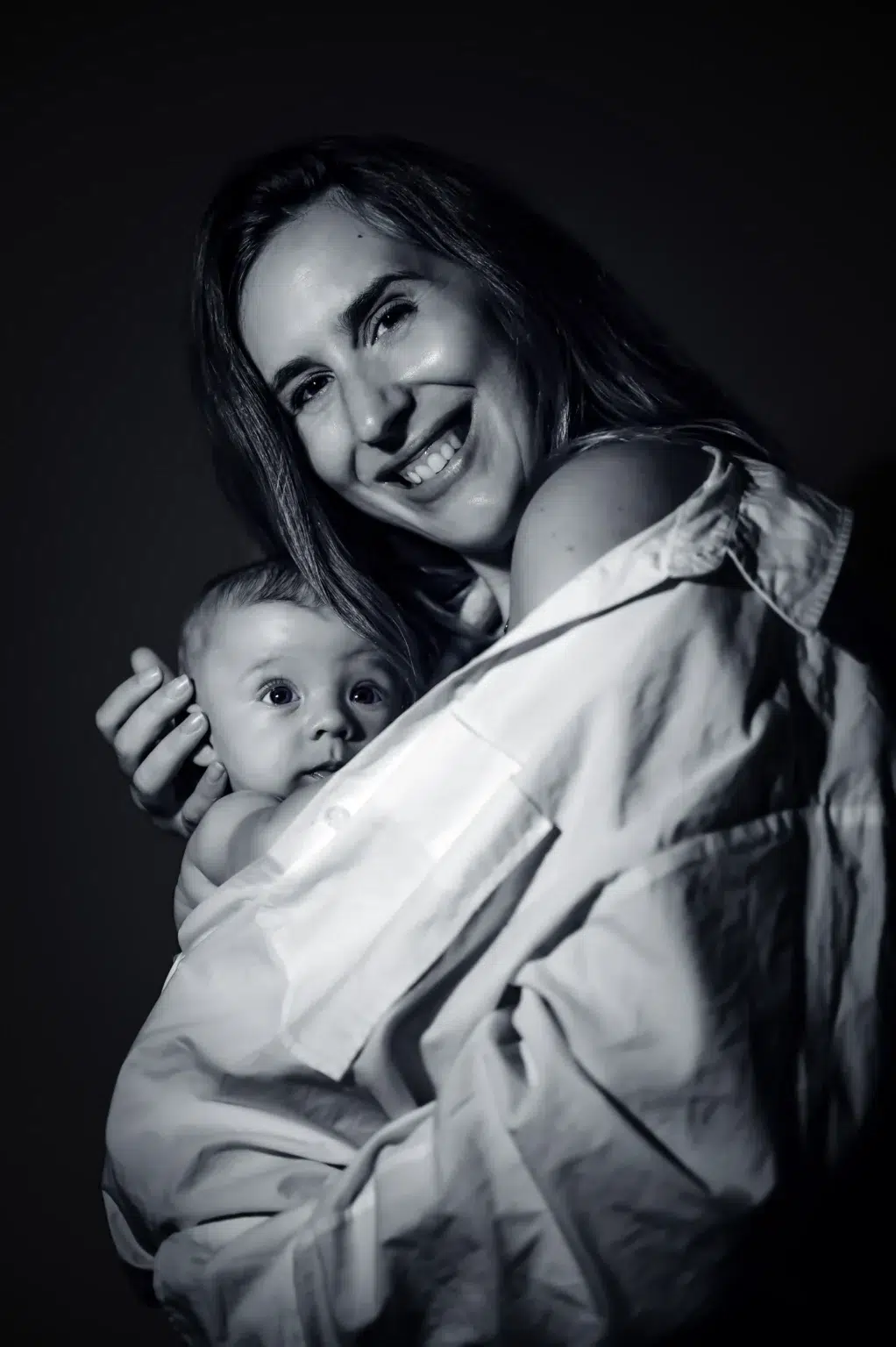 Madre sonriendo mientras sostiene a su bebé durante una sesión en blanco y negro