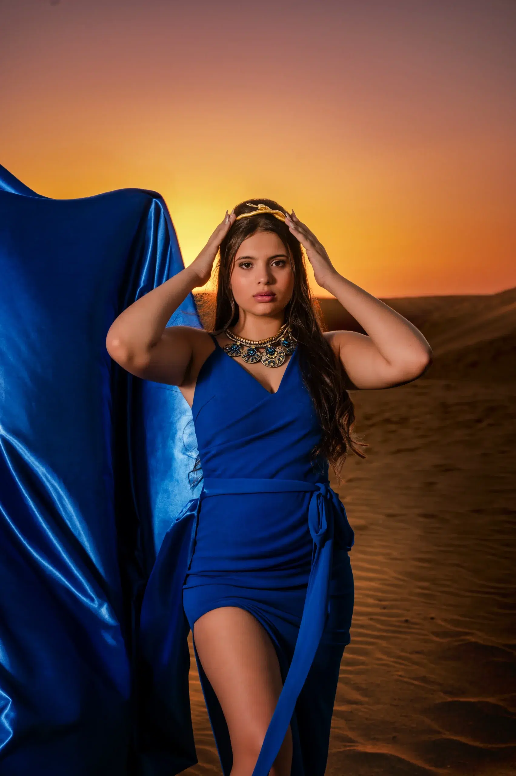 Quinceañera con vestido azul posando con las manos sobre la cabeza en las dunas de Gran Canaria al atardecer