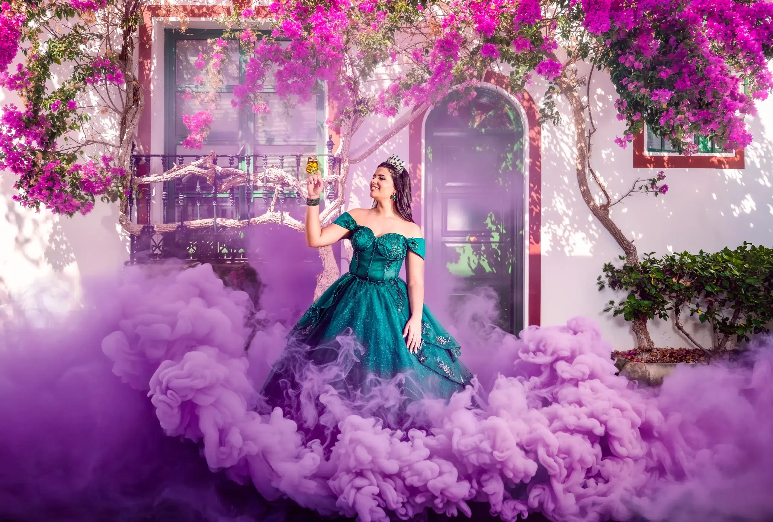 Quinceañera con corona y vestido verde rodeada de buganvillas y humo morado durante una sesión fotográfica en Gran Canaria