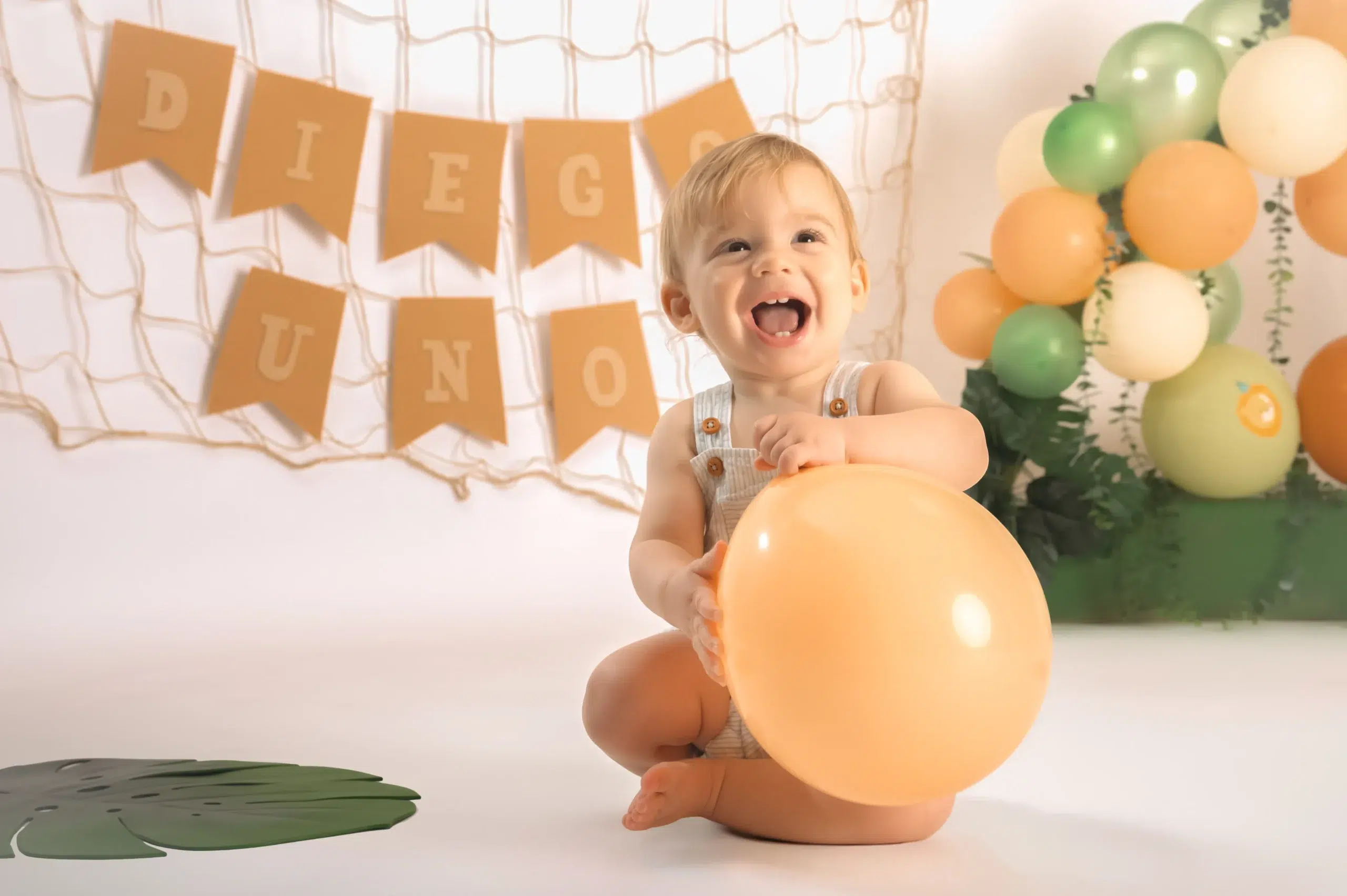 Bebé sonriente sosteniendo un globo naranja durante una sesión Smash Cake de primer cumpleaños en Gran Canaria