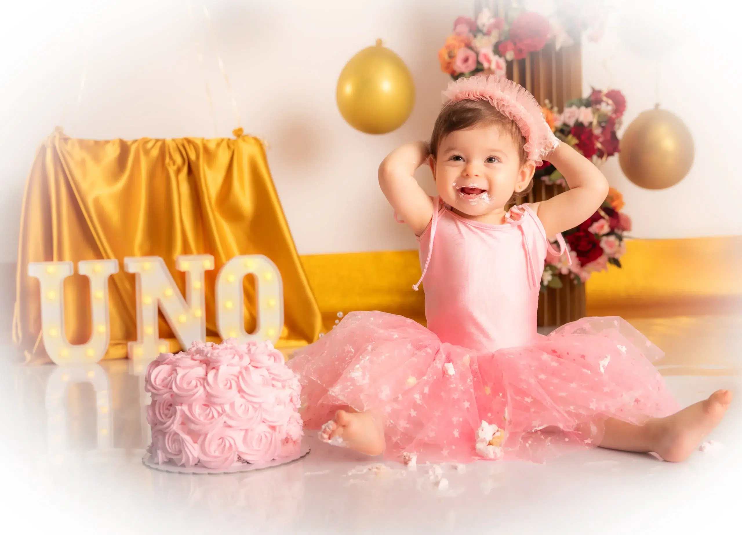 Niña sonriendo con crema en la cara junto a su tarta rosa durante una sesión Smash Cake en Gran Canaria