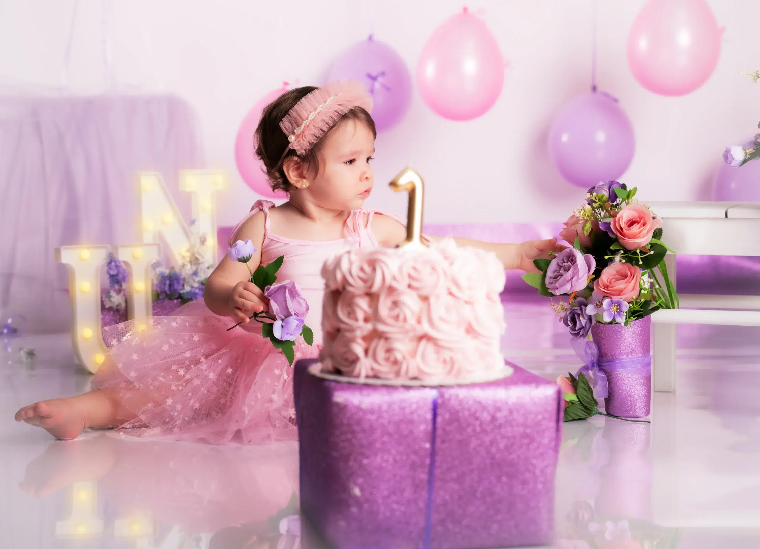 Niña con vestido rosa junto a una tarta de primer cumpleaños y decoración floral durante una sesión Smash Cake en Las Palmas