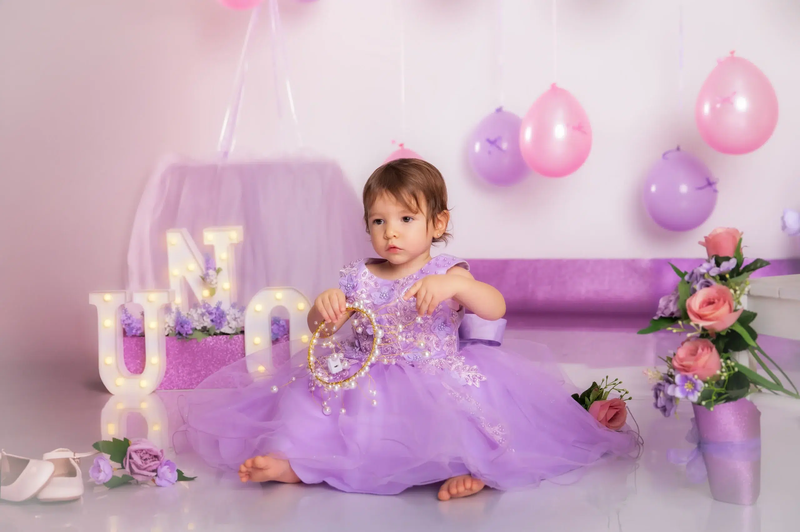 Niña con vestido lila durante una sesión Smash Cake de primer cumpleaños decorada con globos y flores en Las Palmas de Gran Canaria