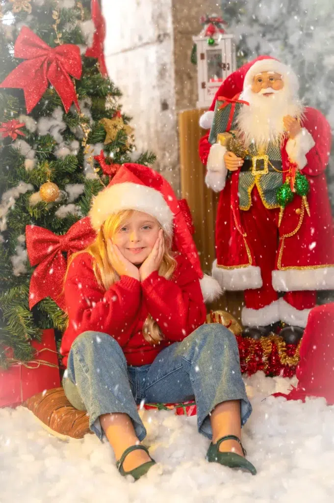 Niña con gorro de Navidad junto a una figura de Papá Noel.
