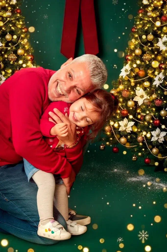 Padre abrazando a su hija junto a un árbol de Navidad iluminado.