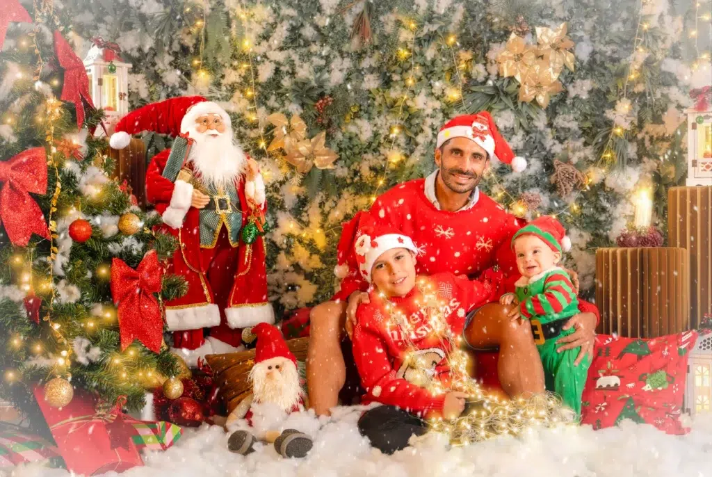 Padre con sus hijos en un decorado navideño con árbol y Papá Noel.